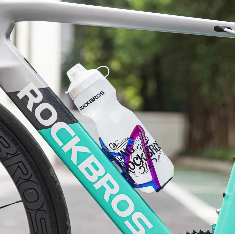ROCKBROS portavasos ligero para bicicleta degradado azul morado montado en cuadro de bicicleta con botella en entorno exterior.