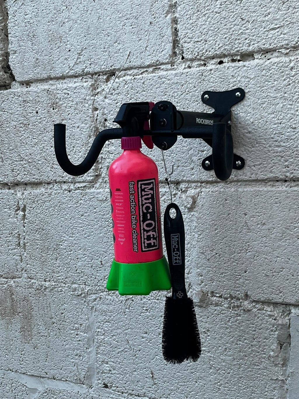 ROCKBROS soporte de pared para bicicleta fijado en pared de ladrillo con productos de limpieza colgados.